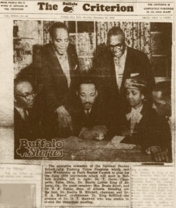 In a yellowed newspaper photo, Dr. Martin Luther King sits at a desk surrounded by members of the Faith Baptist Church