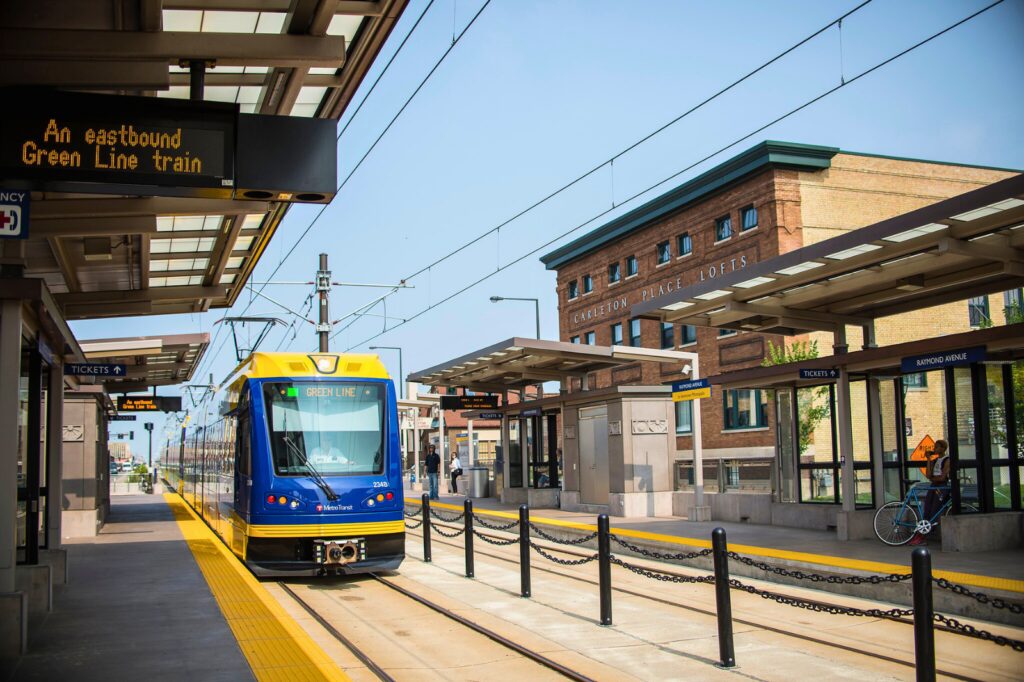 An eastbound Green Line train pulls into a station alongside apartment buildings.