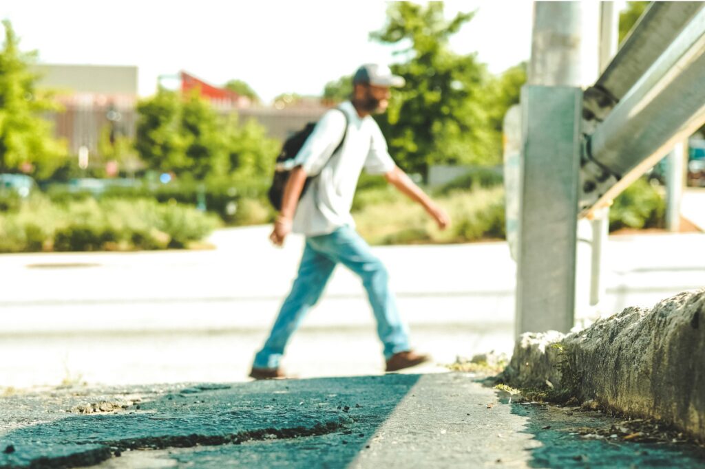 A man in jeans and a white t-shirt walks along the side of a wide, sunny street