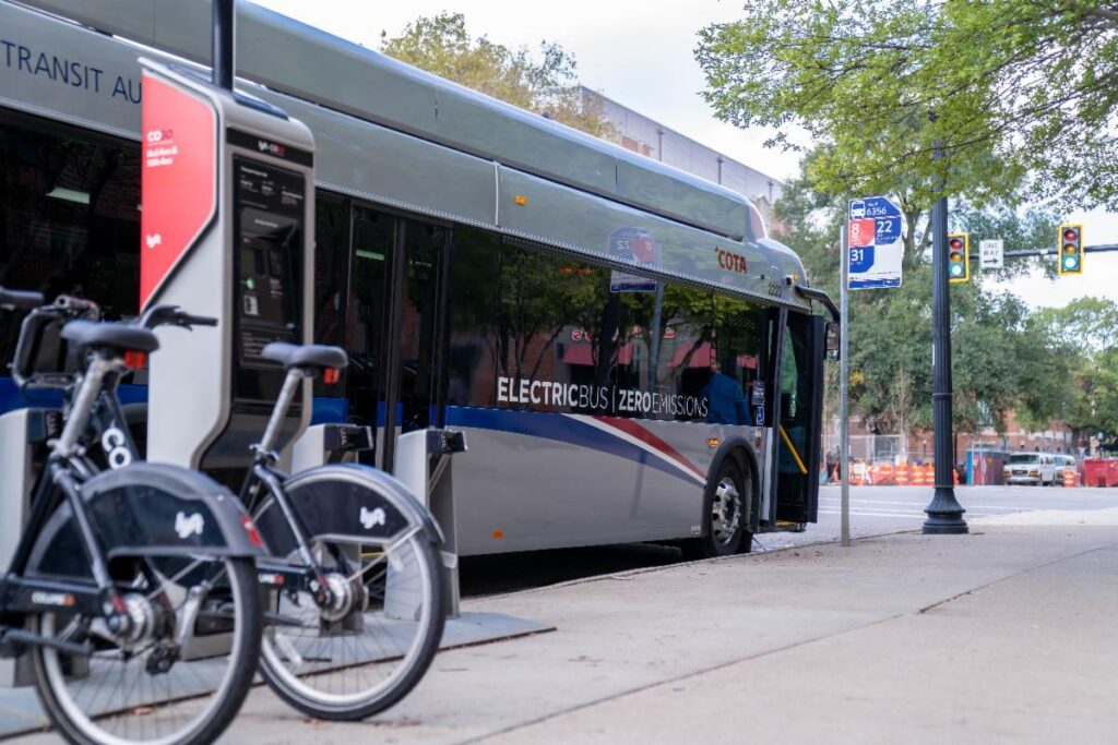 An electric Central Ohio bus arrives at a stop with a nearby bikeshare station